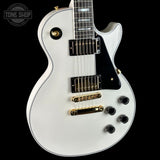 White electric guitar with gold hardware on a black background, featuring the Tone Shop logo.