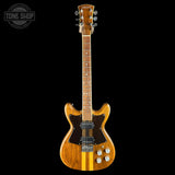 A classic electric guitar with a natural wood finish and two vertical gold stripes, shown against a solid black background. A Tone Shop watermark is visible in the top-left corner.