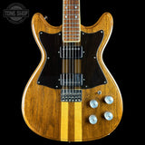 A double-cutaway electric guitar with a natural wood body, black pickguard, and two vertical gold stripes on the lower bout, shown against a black background with a Tone Shop watermark in the top left corner.
