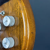 Close-up of a wooden electric guitar body with silver control knobs against a dark blue-gray background.