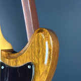 Close-up of a glossy brown wooden electric guitar body with a black pickguard and part of the neck visible against a dark blue-gray background.