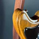 Close-up of a glossy brown wooden electric guitar body with a black pickguard and part of the neck, photographed against a dark gray background.