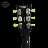 Close-up of the headstock of a black electric guitar against a black background, showing six yellow tuning pegs and gold printed text including 'Vintage' and 'Vintage a John Hardy Strings Product'.
