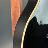 Close-up detail of a glossy black electric guitar body with a light cream binding edge, showing a small defect on the finish.