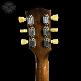 Close-up of the headstock of a guitar against a black background, showing six silver tuning pegs with cream-colored knobs and the brand name 'Gibson' visible on the pegs.