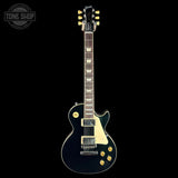 A black electric guitar with gold hardware and a cream pickguard, shown vertically against a solid black background. A 'TONE SHOP' watermark is visible in the top-left corner.