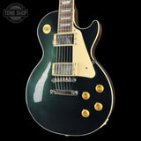 A black electric guitar with a glossy dark greenish-black finish, cream pickguard, and gold hardware, shown against a black background with a Tone Shop watermark in the top left corner.