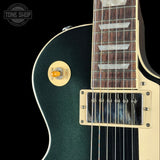 Close-up of a dark green electric guitar body with a cream pickguard, black humbucker pickups, and a dark wood fretboard, shown against a black background with a Tone Shop watermark.