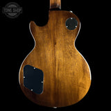 The back of an electric guitar with a glossy brown wood finish, featuring a cutaway body shape, black pickguard, and black circular control cover, shown against a solid black background.