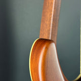 Close-up detail of a wooden instrument body corner meeting the neck, showing a warm reddish-brown wood finish and a light cream edge against a dark gray background.