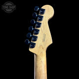 Close-up rear view of a guitar headstock with six black tuning pegs, a natural wood neck, and visible 'Fender' branding on a black background.