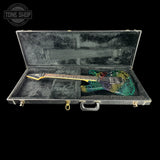 An electric guitar with a vibrant multicolor mosaic body design resting inside an open black hard case with gray velvet lining, set against a solid black background.