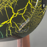Close-up of a glossy black guitar body featuring a bright yellow lightning-bolt crackle pattern and a small chip with exposed wood showing through the cracked finish.