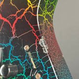 Close-up of an electric guitar body featuring a black base with a vibrant, multicolor crackle pattern in red, orange, yellow, green, and blue, with a clear plastic switch and metal controls.