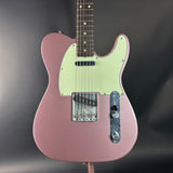Pink electric guitar with a light green pickguard on a dark gray background