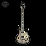 A double-cutaway electric guitar with a glossy flamed maple body, featuring a natural wood burst finish, gold hardware, and a black headstock, shown against a solid black background.