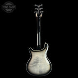 A double-cutaway electric guitar shown from the back, featuring a natural figured maple top with a silver flame finish and a glossy black neck and headstock, set against a solid black background.