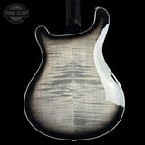 Close-up of the back of an electric guitar body with a glossy black finish, showing the natural wood grain and a white binding edge against a black background.