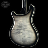 Close-up of the back of an electric guitar body with a flamed maple wood finish, showing a silver-gray burst and natural wood grain against a black background. A Tone Shop watermark is visible in the top-left corner.