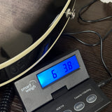 A close-up of a digital smart scale displaying '6 38 kg' in blue LED, placed on a dark wooden surface next to a black guitar body.