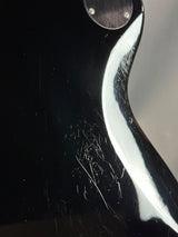 Close-up of a guitar with visible scratches on the black finish