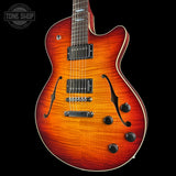 A double-cutaway electric guitar with a vibrant sunburst finish, featuring a bright orange body, dark brown edges, and black hardware, shown against a solid black background with a Tone Shop watermark in the top left corner.