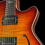Close-up of an electric guitar body showing a sunburst orange and brown flamed maple wood finish, black humbucker pickups, and a cream edge trim against a black background.