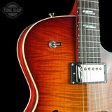 Close-up of an electric guitar body showing a sunburst finish that transitions from bright orange-red to dark brown, with a black pickguard and dark fretboard against a black background.