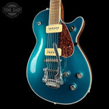 A teal blue electric guitar with a maple body, cherry wood sides, cream humbucker pickups, and a chrome tailpiece, shown against a solid black background with a Tone Shop watermark in the top left corner.