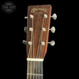 Close-up of the headstock of a Martin & Co acoustic guitar, showing the brand name in gold script on a dark brown wood background, with six silver tuning pegs and strings against a solid black background.