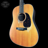A classic acoustic guitar with a natural wood finish and a black pickguard, shown against a solid black background with a Tone Shop watermark in the top left corner.