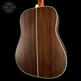 The back of an acoustic guitar with a dark brown wood grain finish and a cream-colored binding, shown against a solid black background with a Tone Shop watermark in the top left corner.