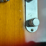 Close-up of a guitar or instrument body with a wood finish and a silver metal control knob mounted on a vertical plate.