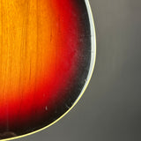 Close-up of a sunburst electric guitar body corner showing the orange, red, and black wood finish gradient with a light gold edge.