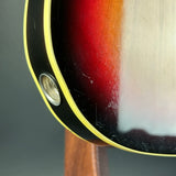 Close-up detail of an electric guitar body showing a sunburst finish transitioning from black to red and orange, with a yellow binding edge and a visible gold-toned hardware eyelet.