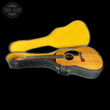 An acoustic guitar with a natural wood body and dark neck, resting inside an open black hard case with a bright yellow foam lining, shown against a solid black background.