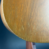 A close-up detail shot of a wooden object, showing a warm medium-brown wood grain surface with a curved edge and a dark blue background.