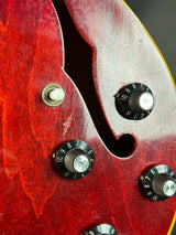 Close-up of a red electric guitar with control knobs on a dark background