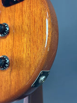 Close-up of a wooden guitar headstock with tuning pegs against a blue background