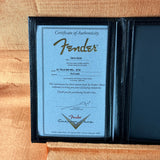 A Fender Certificate of Authenticity document displayed inside a black leather-bound case on a tan textured fabric background.