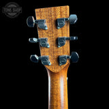 Close-up of the headstock of a guitar with a warm brown wood finish and black tuners, shown against a solid black background. A Tone Shop watermark is visible in the top left corner.