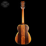 The back of an acoustic guitar made of rich, dark wood grain, shown against a solid black background with a Tone Shop watermark in the top left corner.