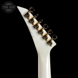 Close-up of the headstock of an electric guitar with a glossy white body and gold tuning pegs, shown against a solid black background. A Tone Shop watermark is visible in the top-left corner.