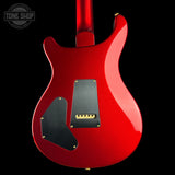 The rear view of a glossy red electric guitar body against a solid black background, featuring black pickguards and gold hardware.