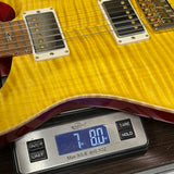 Close-up of a yellow flamed-top electric guitar resting on a digital scale displaying 7.80 lbs.