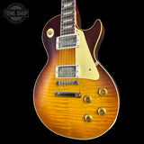 A classic electric guitar with a natural flamed maple top showing a vibrant sunburst gradient from amber-orange to dark brown. It features a cream pickguard, dual humbucker pickups, and gold-toned hardware, set against a solid black background.