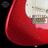 Close-up of a red glitter electric guitar body with a white pickguard and chrome bridge against a black background. A Tone Shop watermark is visible in the top-left corner.