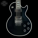 A black electric guitar with a glossy finish, chrome hardware, and white binding, shown against a solid black background with a Tone Shop watermark in the top-left corner.