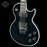 A black electric guitar with white binding and chrome hardware, shown from a side angle against a black background. A Tone Shop watermark is visible in the top-left corner.