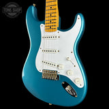 A blue electric guitar with a white pickguard and maple neck, photographed against a solid black background. A Tone Shop watermark is visible in the top-left corner.